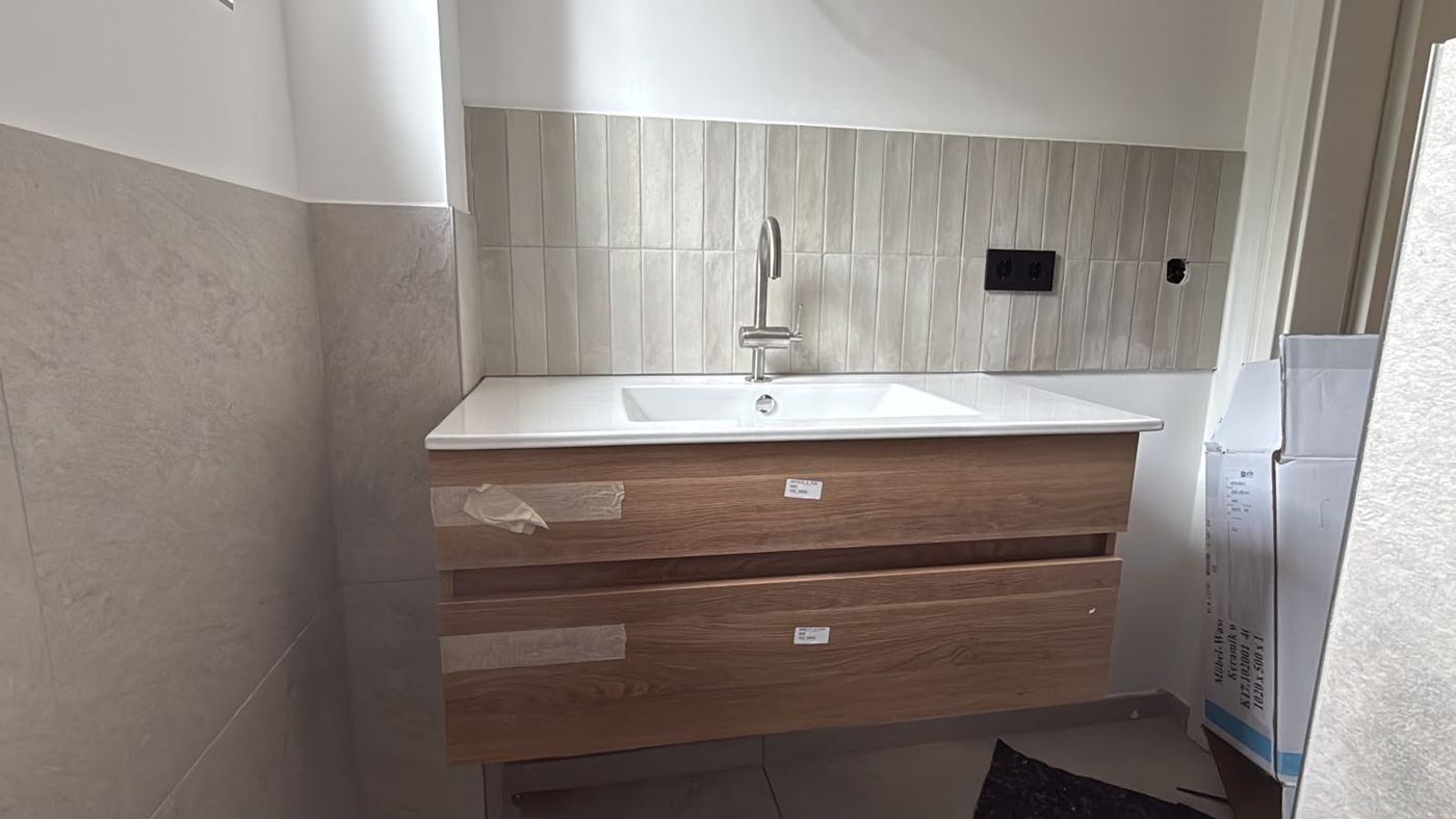 Eingebauter Waschtisch mit Holzfront, Fliesen und Armatur in einem Badezimmer